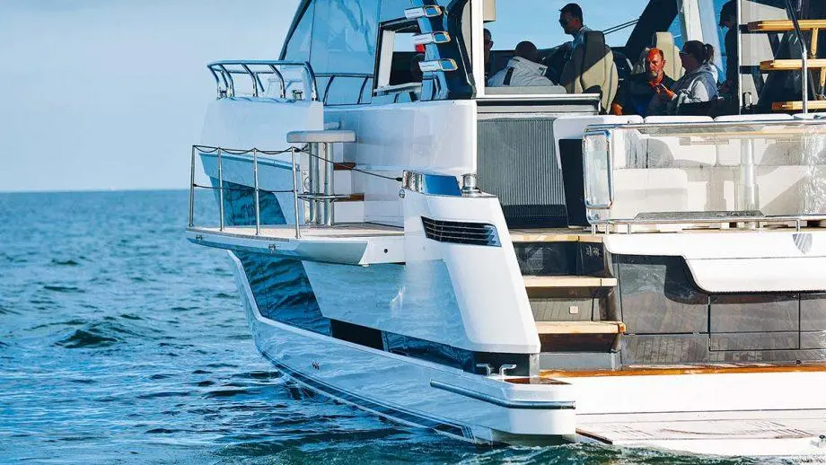 A sleek yacht glides through calm waters with passengers enjoying the view on deck, showcasing elegant design and luxury.